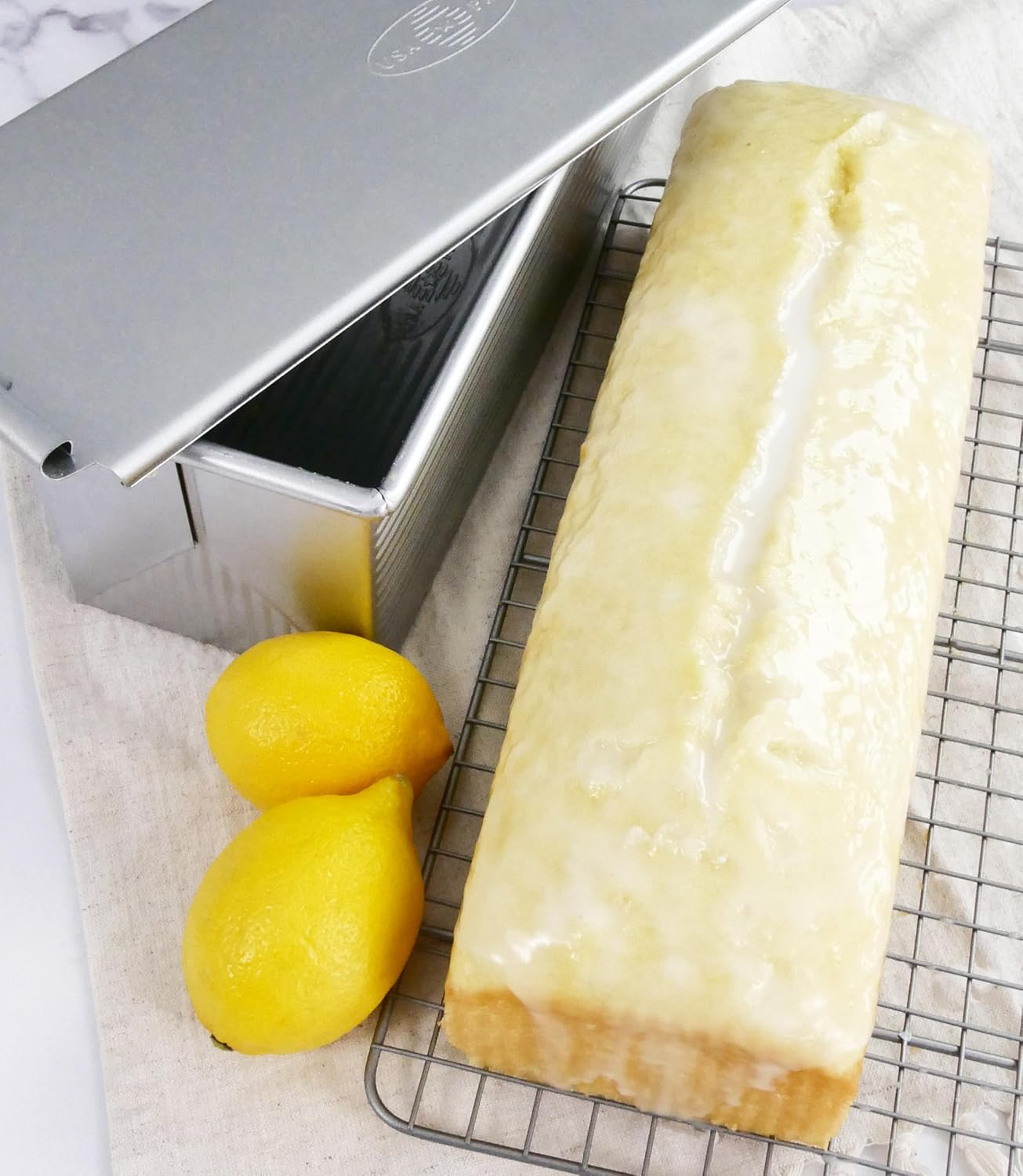 USA Pan 1160PM Pullman pan with the lid partly slid open beside a finished rectangular loaf on a cooling rack.