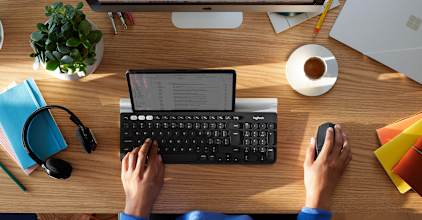 Black Logitech M720 Triathlon used at a multi-device desk beside a keyboard and tablet