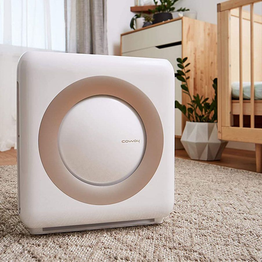 White Coway AP-1512HH air purifier positioned on carpet in a bedroom beside a crib