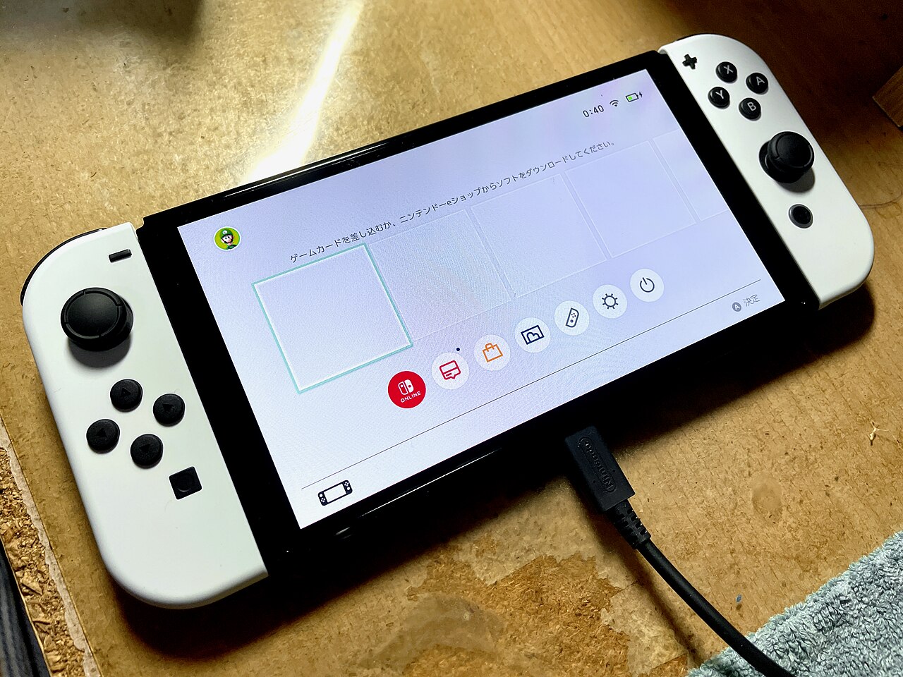 White Nintendo Switch OLED with both Joy-Con controllers attached and the Japanese-language Home menu on screen.