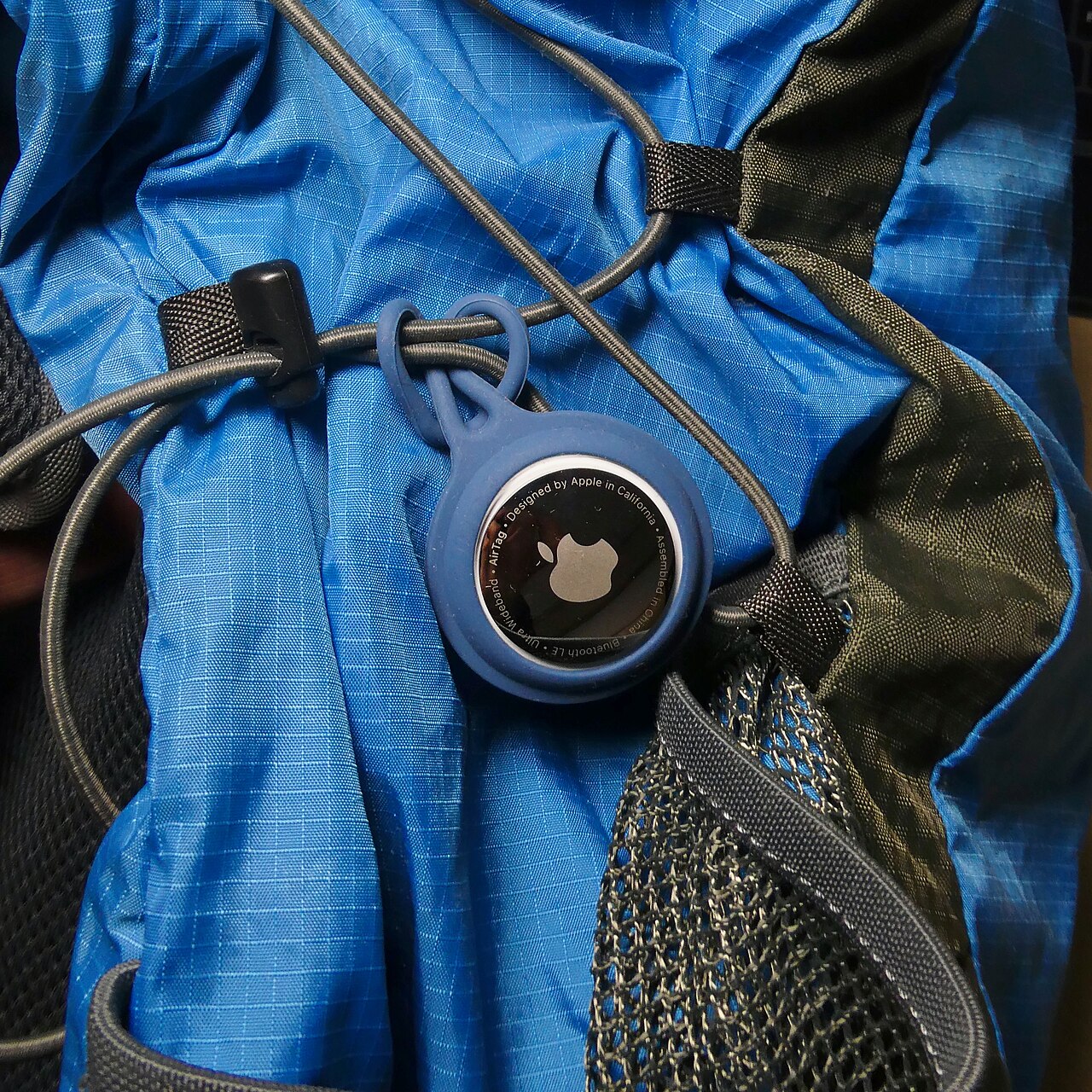 First-generation Apple AirTag in a blue holder attached to a blue backpack.