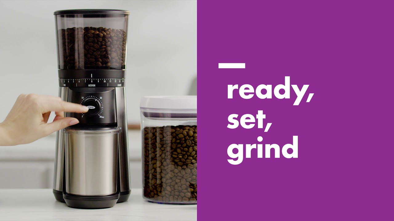 Second OXO official video frame showing the stainless Conical Burr Coffee Grinder and bean hopper