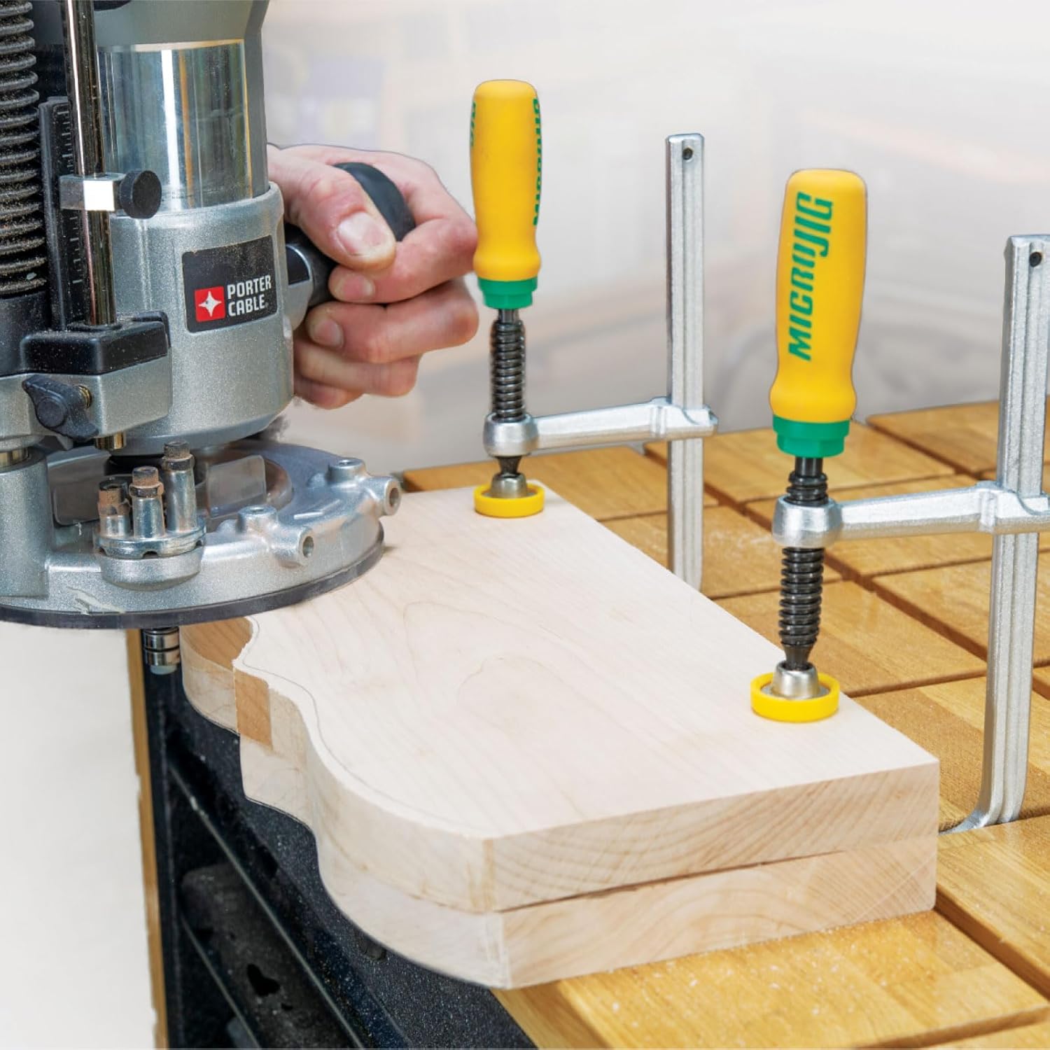 两只 MICROJIG MATCHFIT 夹具在开槽工作台上压住木件，旁边有一台手持木工铣机