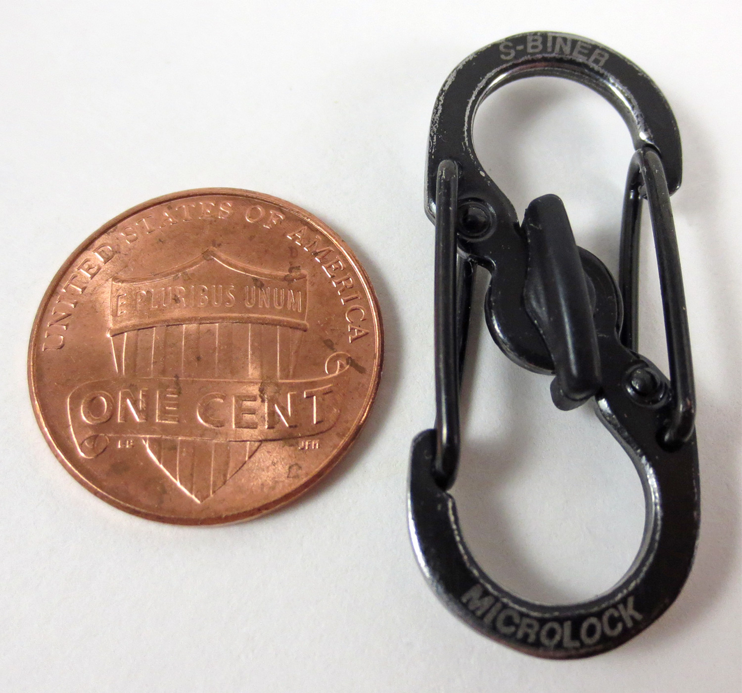 Used black MicroLock beside a penny, with the center lever unlocked while both wire gates remain closed.