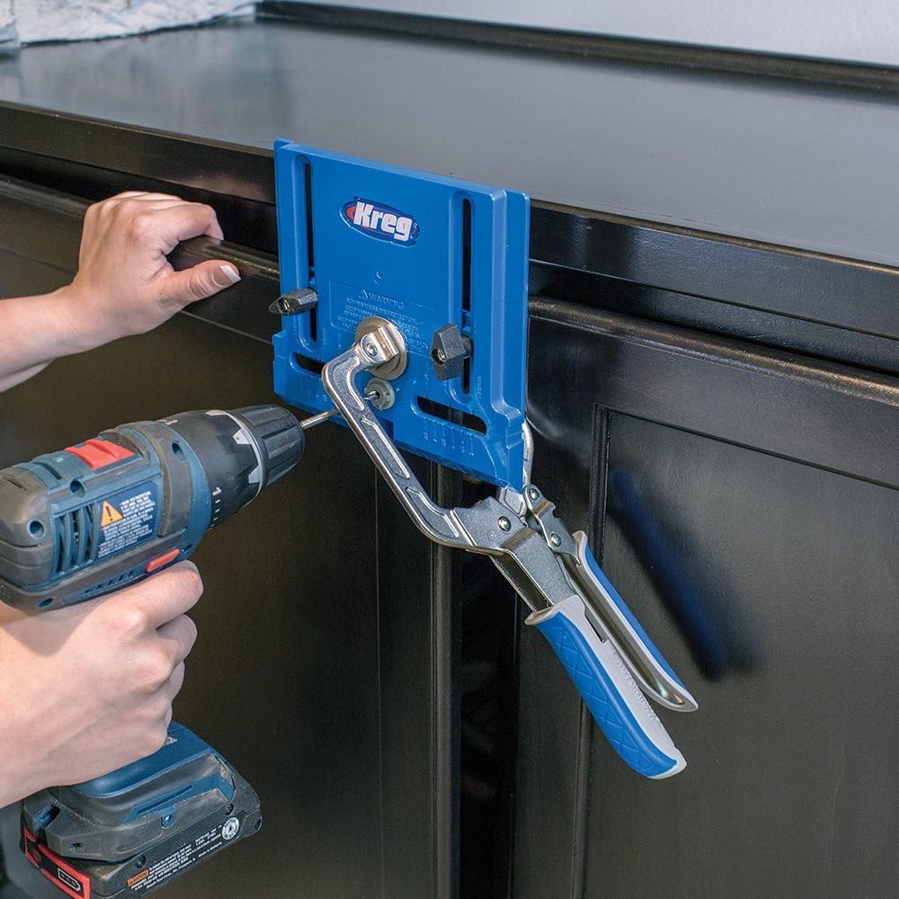 Blue Kreg KHI-PULL jig clamped to a black cabinet front, with a drill bit entering a steel guide.