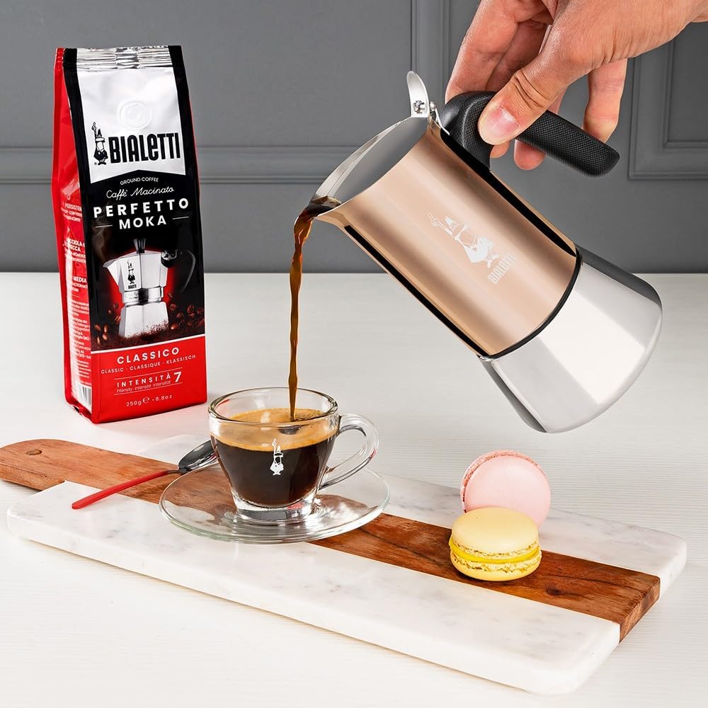 Supplier photograph of a hand pouring from a copper Bialetti Venus into a small glass coffee cup