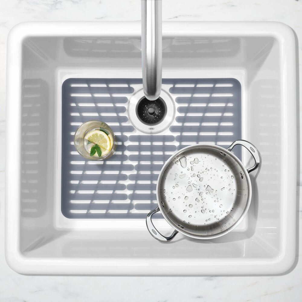 OXO Large Silicone Sink Mat in a white sink with an opening around a rear drain, a glass and a saucepan