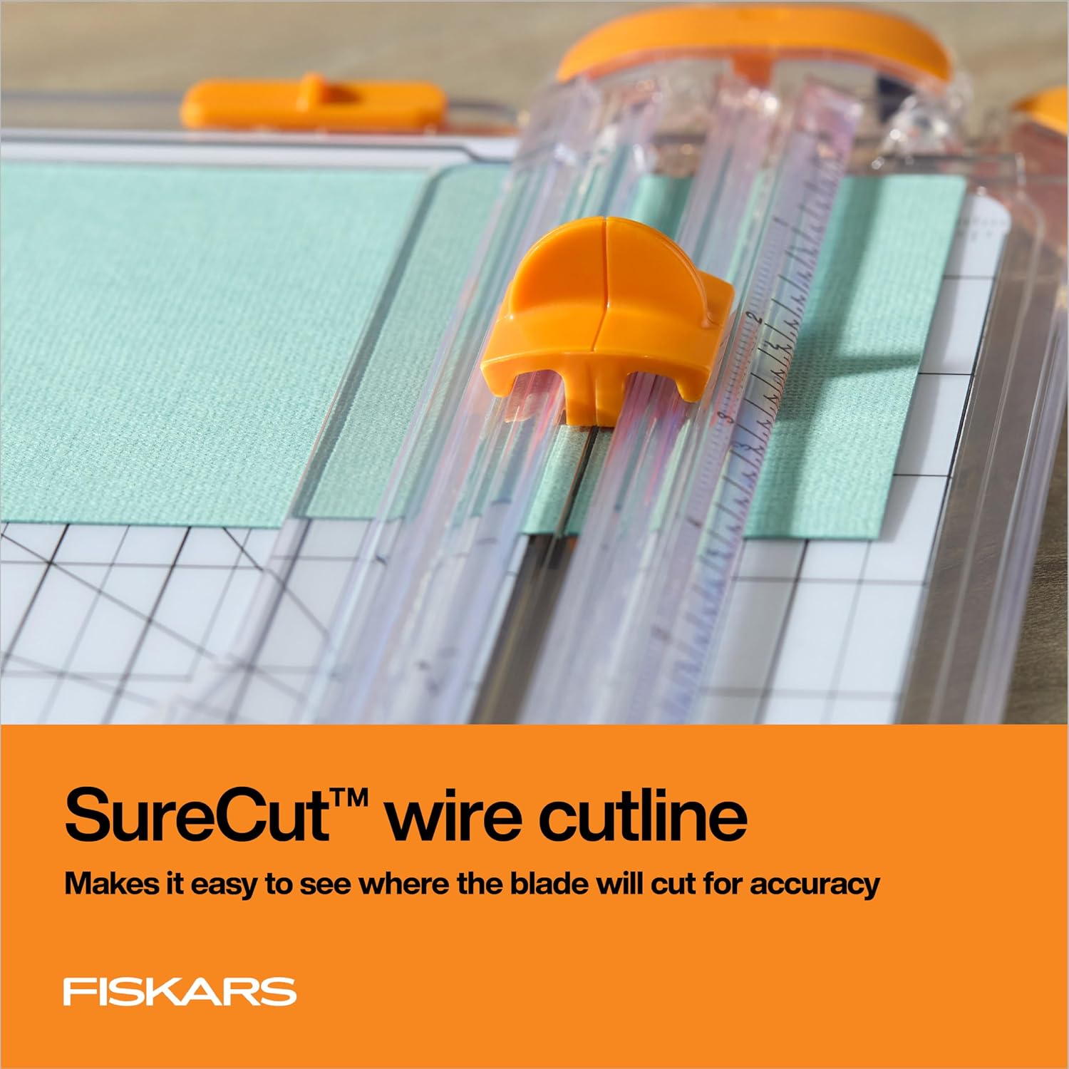 近景展示橙色刀座、透明导轨，以及位于蓝绿色纹理纸上方的 SureCut 钢丝。