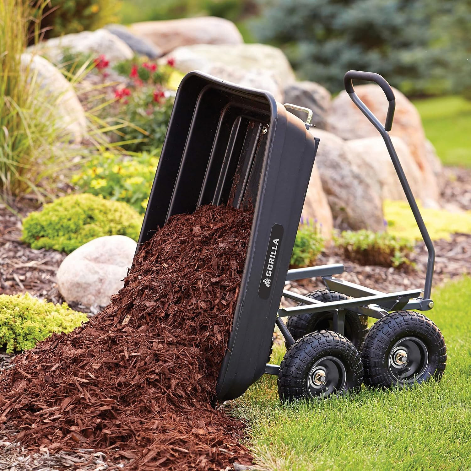 The Gorilla GOR4PS tub tipped upward with reddish-brown mulch pouring onto the ground beside a planted border.