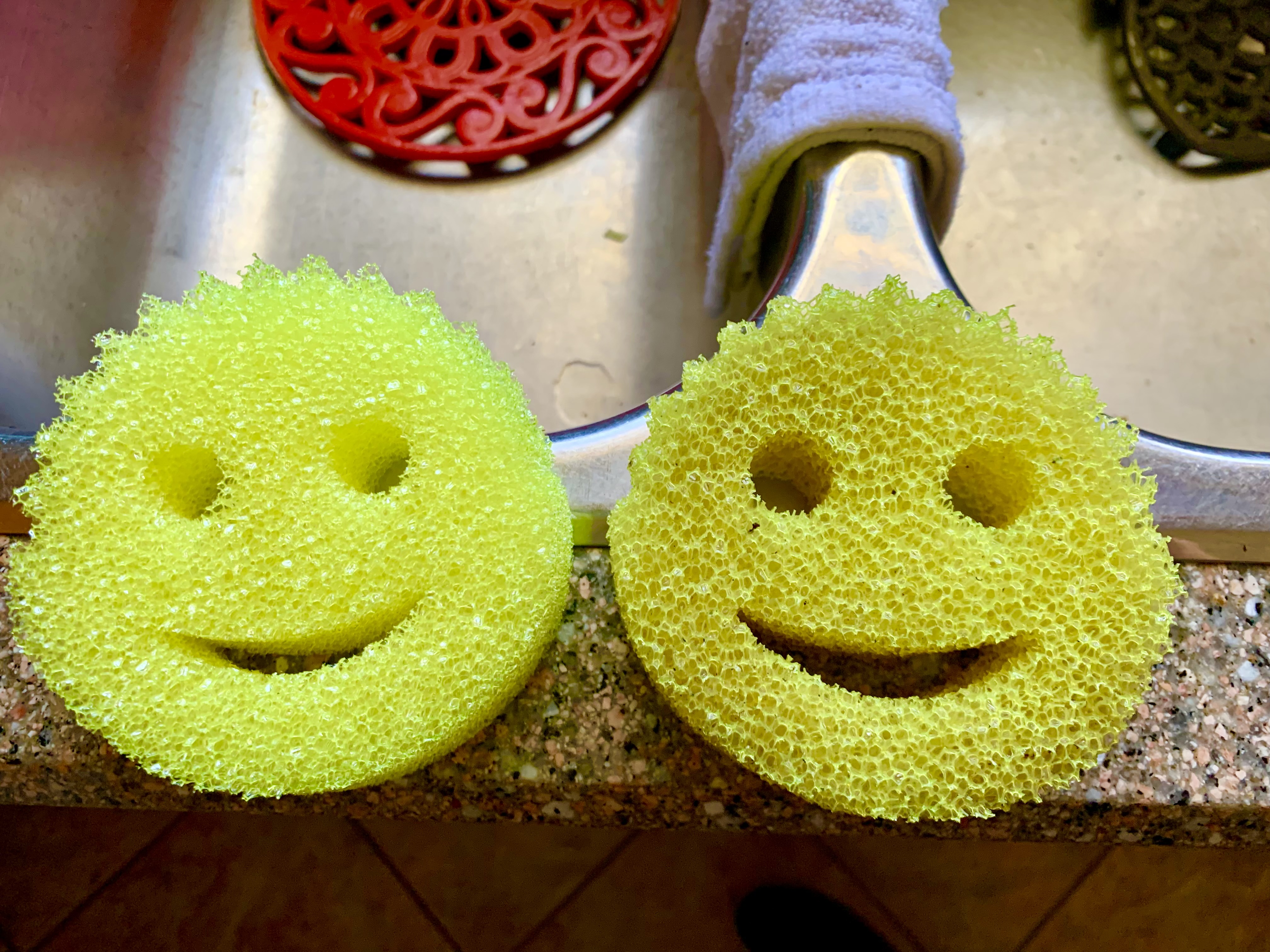 Two yellow smile-shaped scrubbers, one newer and one older, beside a sink