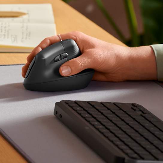 Right hand resting on the Graphite Logitech Lift Vertical Ergonomic Mouse beside a keyboard