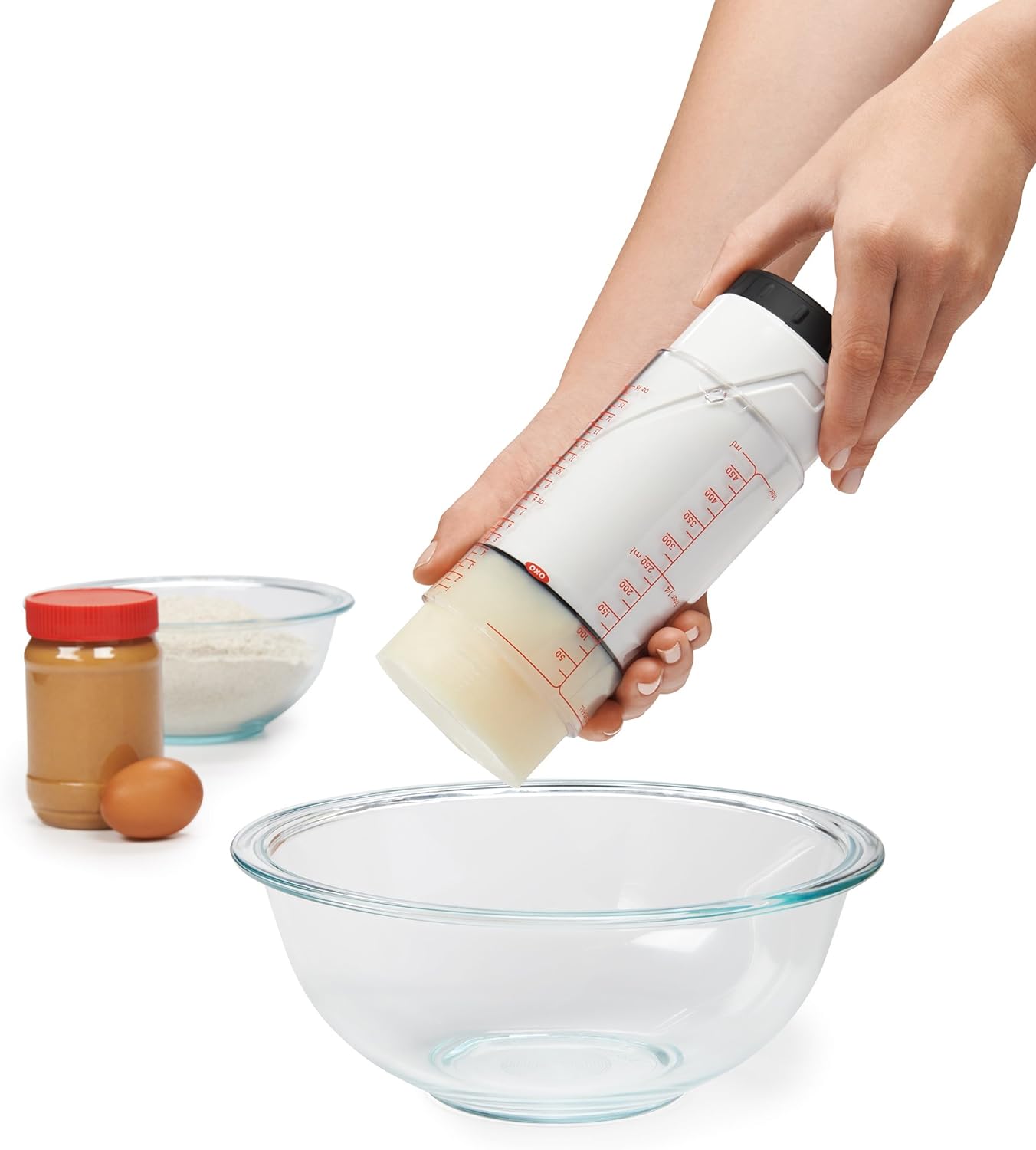 双手操作 OXO 两杯可调量杯，将黏稠食材推出杯口并移向搅拌碗