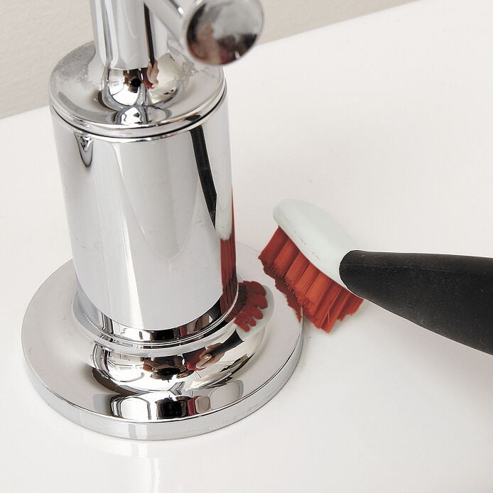 The smaller OXO brush positioned beside a faucet.