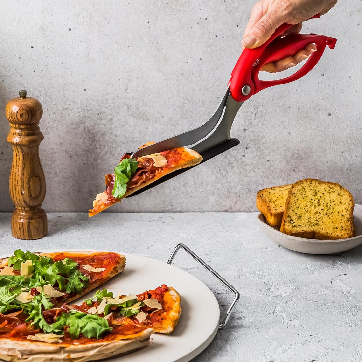 A hand uses red Dreamfarm Scizza pizza scissors to lift a freshly cut pizza slice.