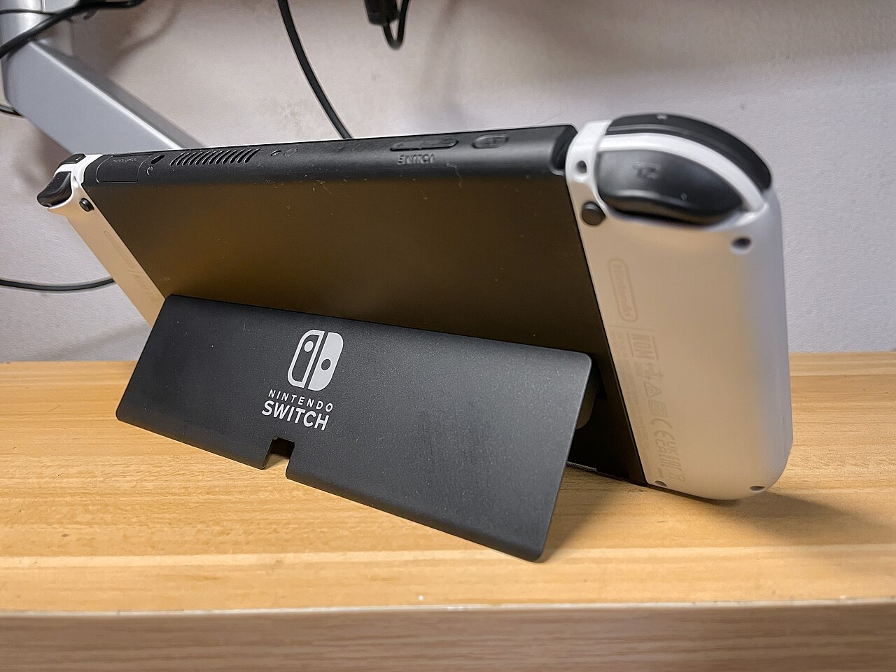 Rear view of a white Nintendo Switch OLED standing on its wide built-in kickstand.