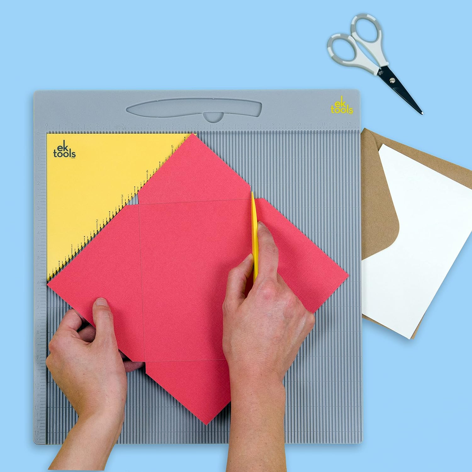 Supplier demonstration of red paper aligned diagonally on the scoring board while a hand uses the yellow bone folder