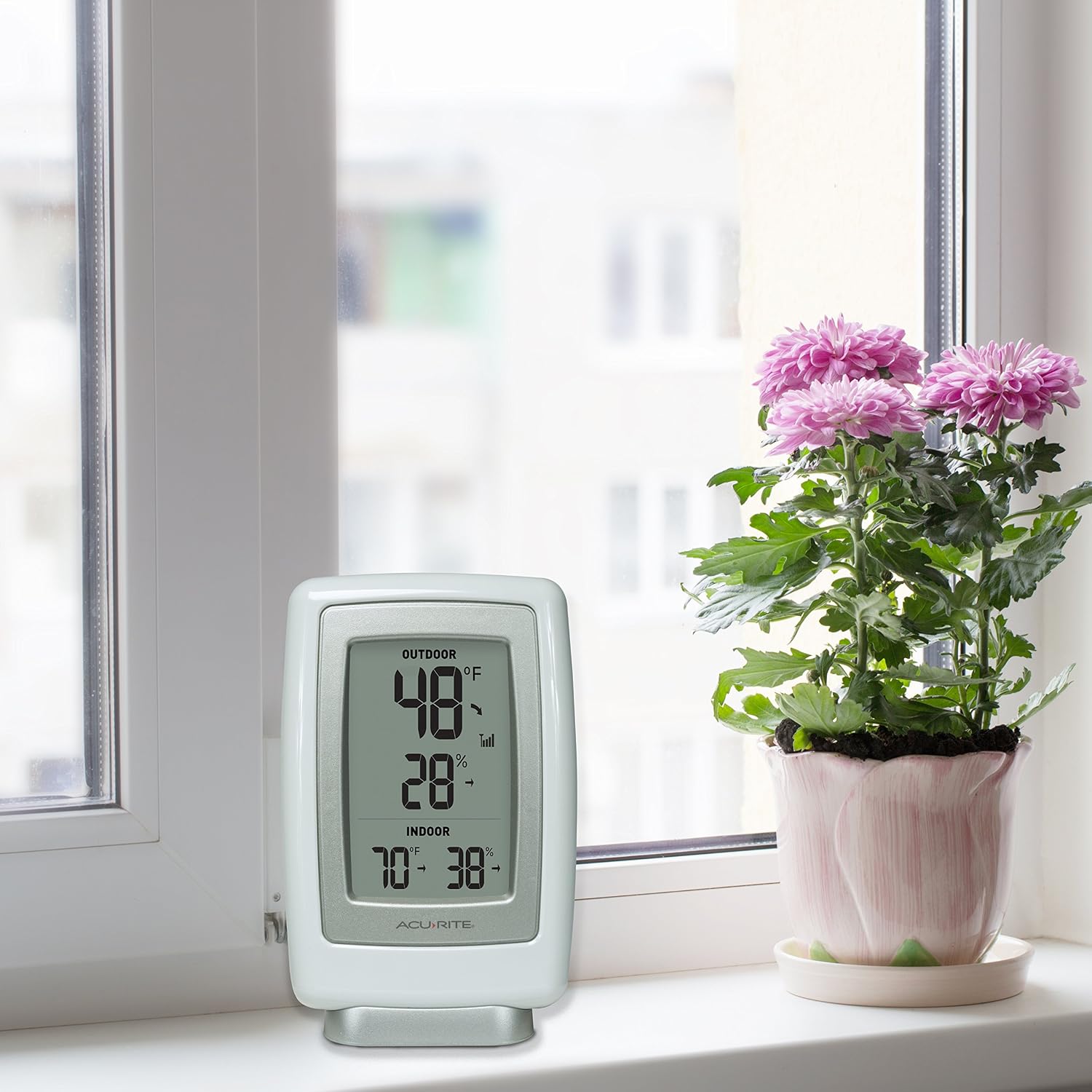AcuRite display standing on its base on a windowsill beside a flowering plant in the listing's use image.
