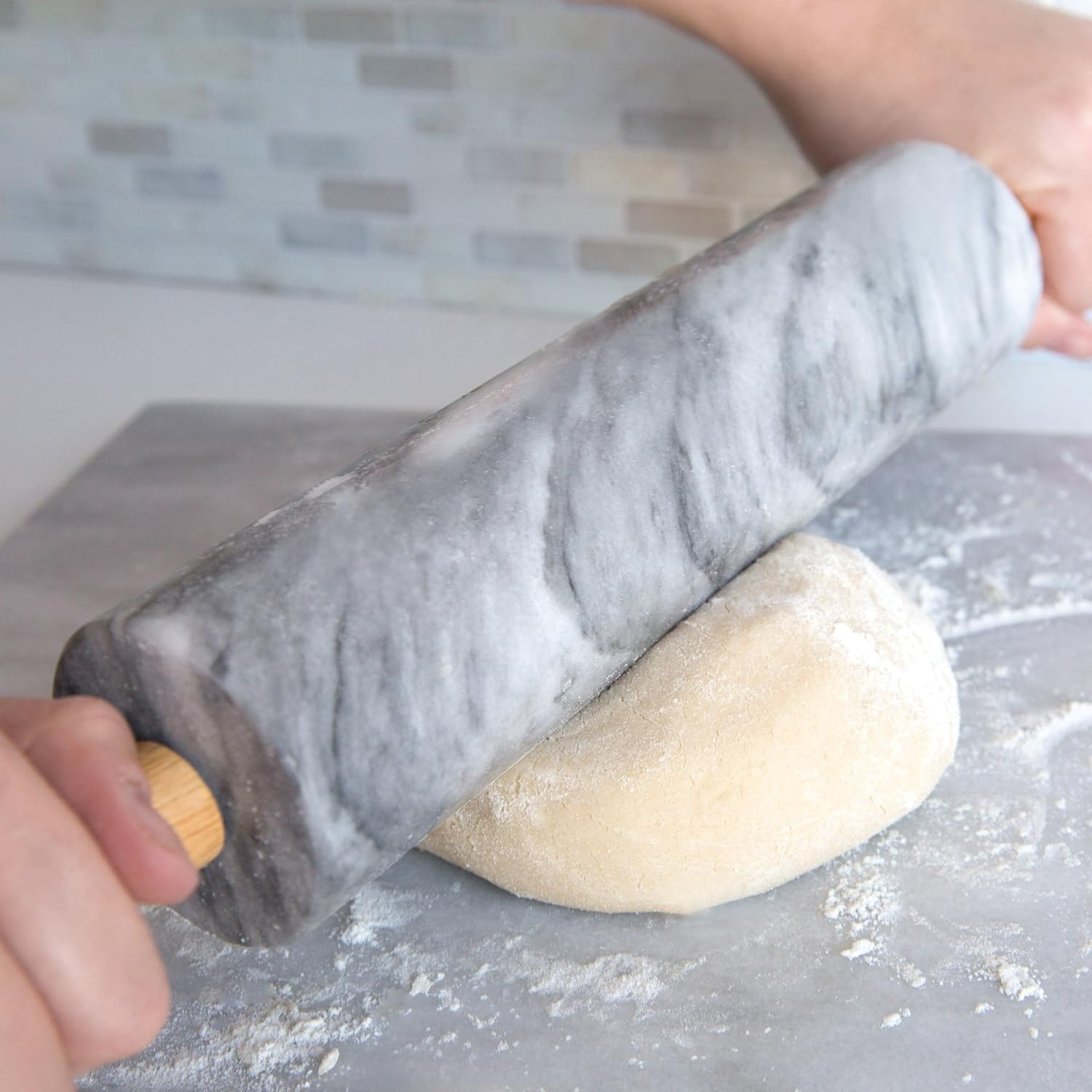 Hands holding a marble rolling pin by its wooden handles over dough on a floured work surface