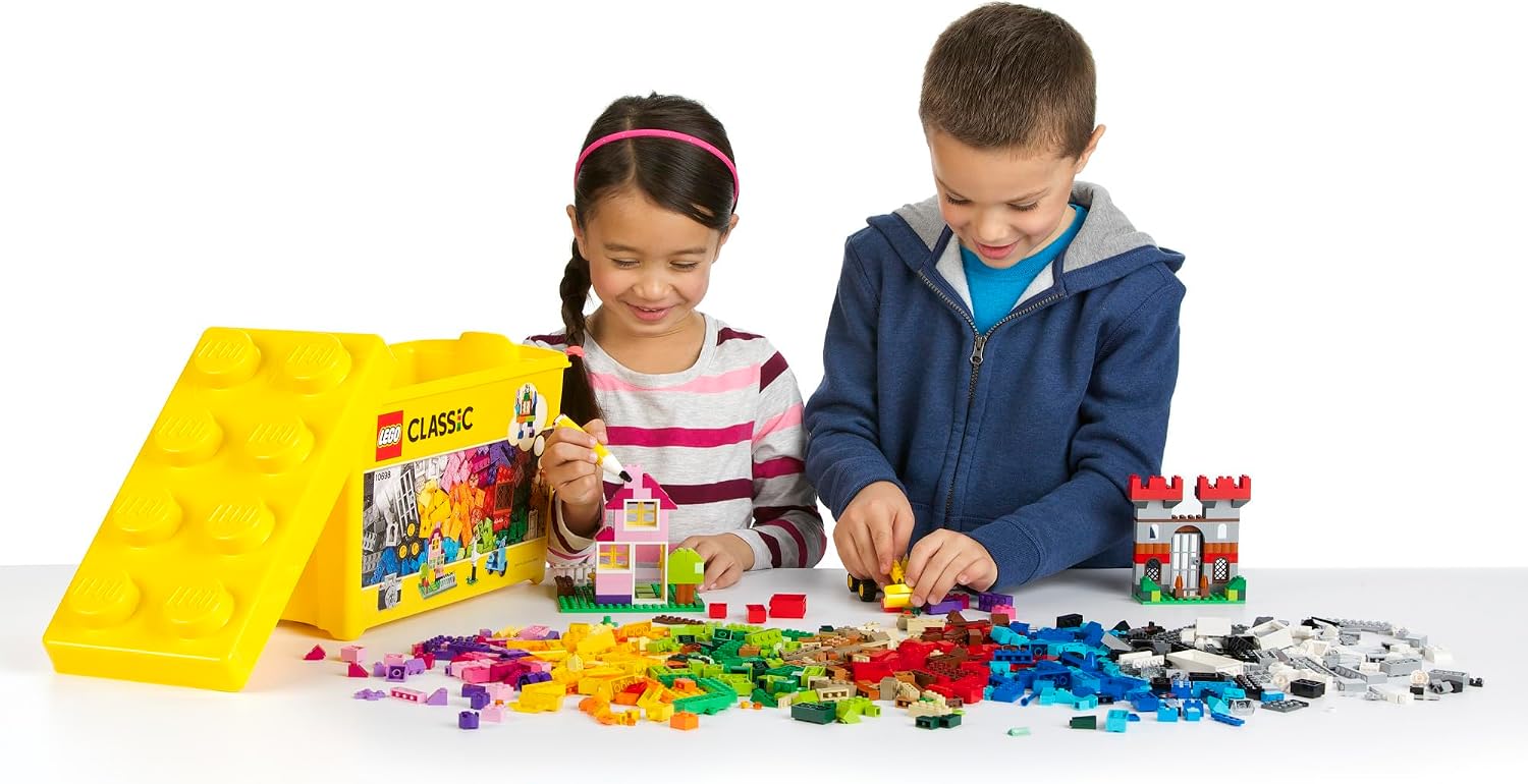 Two children building beside an open yellow LEGO Classic 10698 box, with loose bricks spread across a table