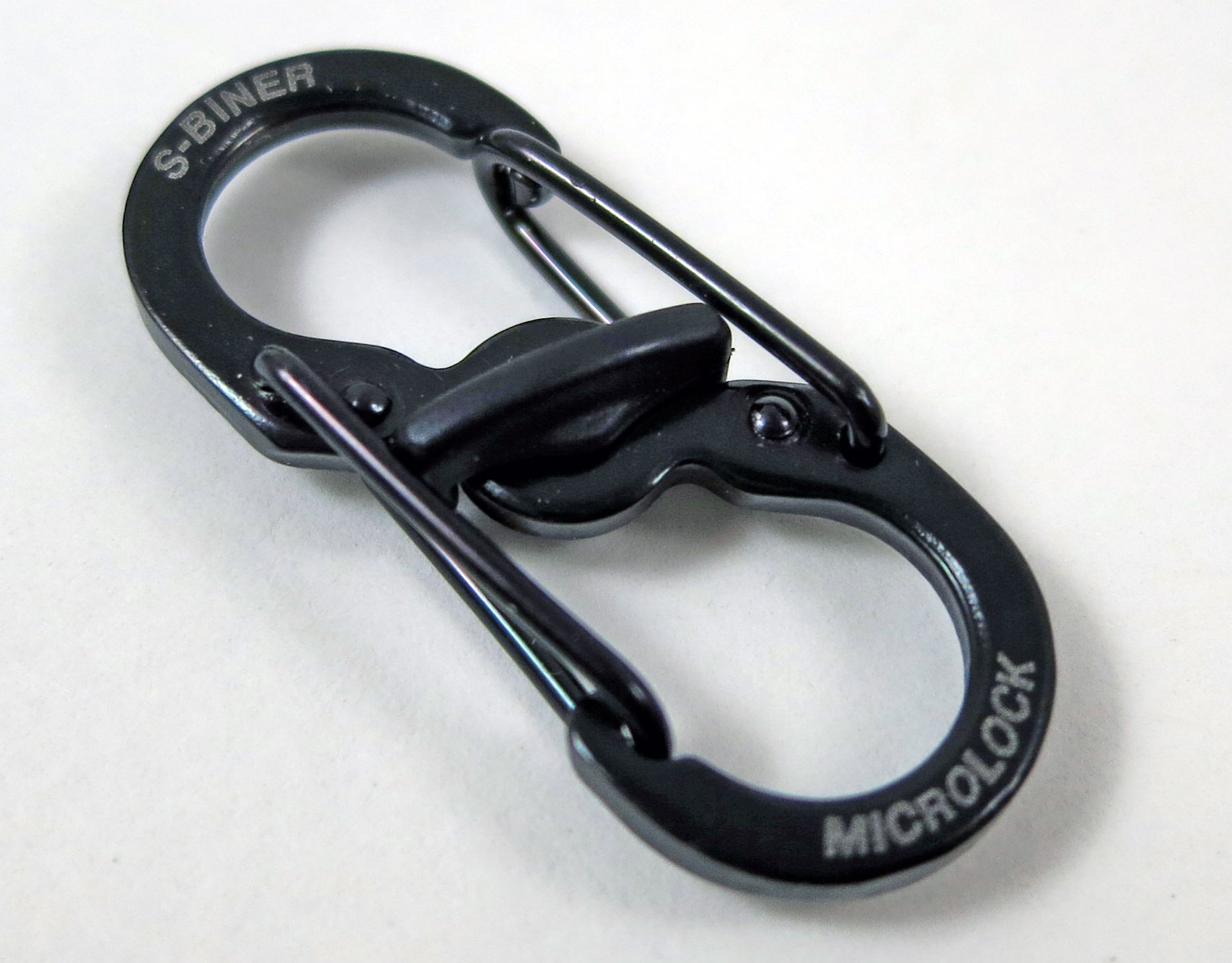 One used black Nite Ize MicroLock with older lettering and its center lever blocking both wire gates.