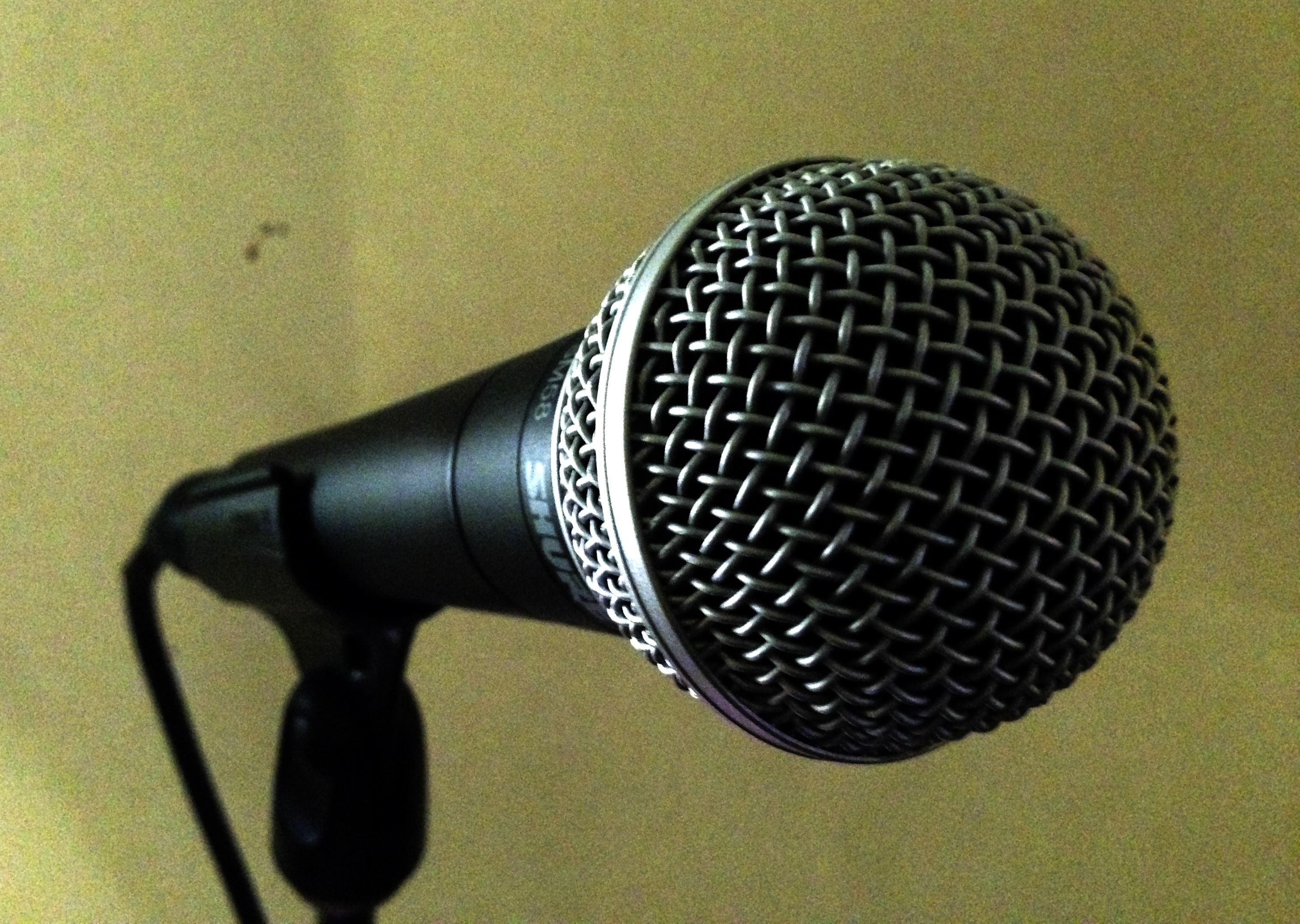 Wired Shure SM58 held in a stand clip with a cable connected at the rear, viewed toward its silver grille.