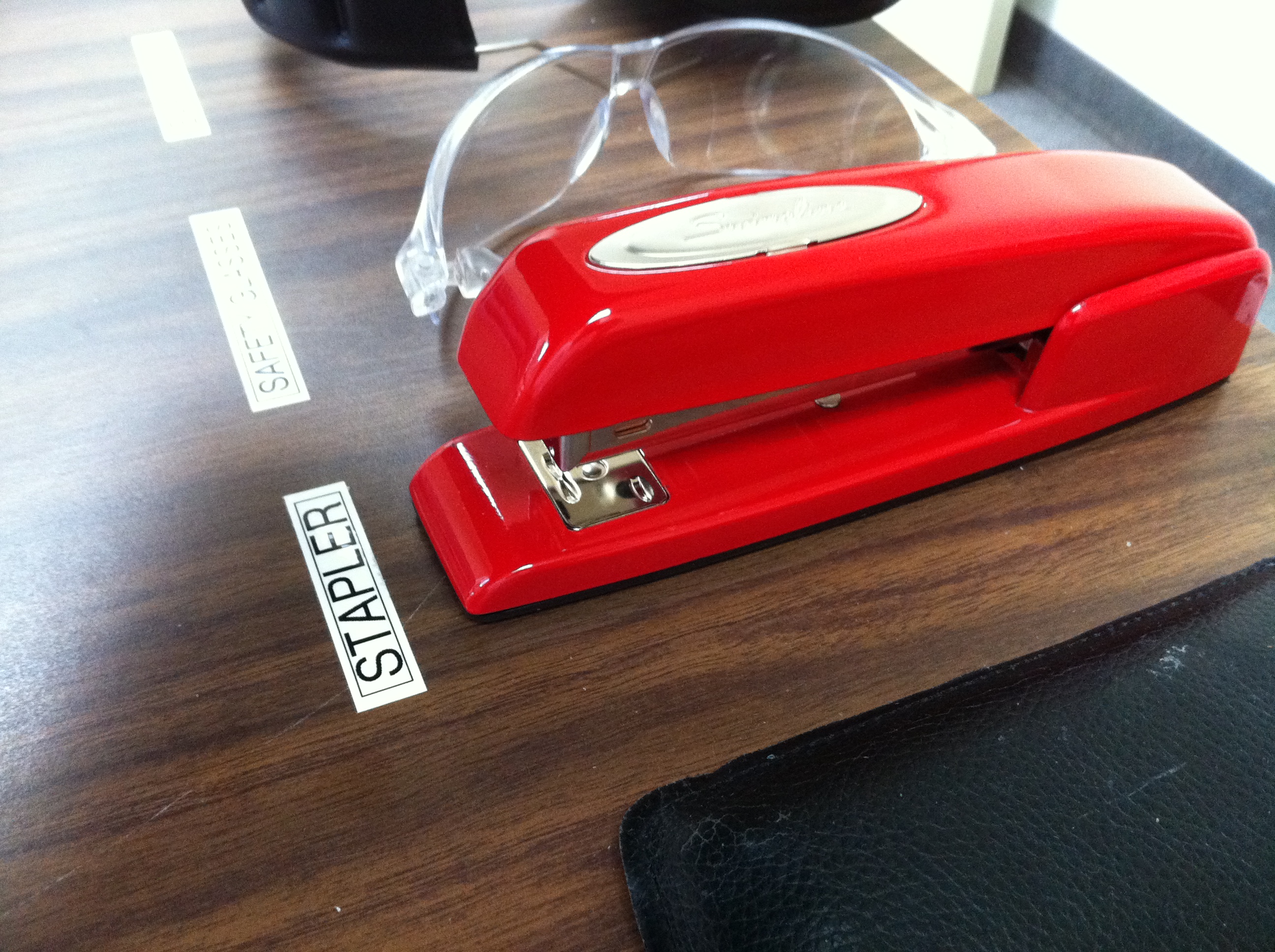 Rio Red Swingline 747 on a work surface beside a stapler label and safety glasses